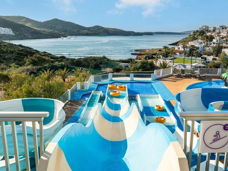 Blauwe en witte glijbaan met uitzicht op een kustplaats en oceaanbaai onder een heldere hemel.