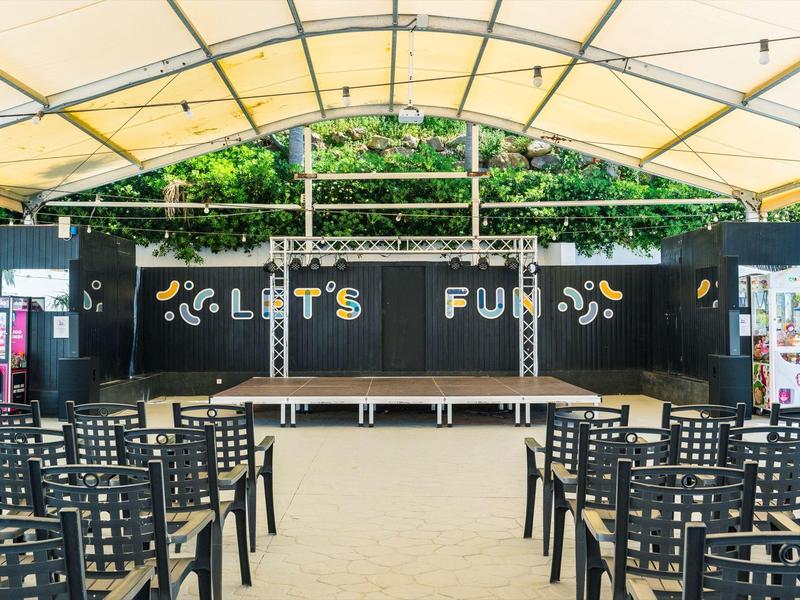 Buitentheater met zwart decor en zitplaatsen onder een gele doorzichtige luifel.