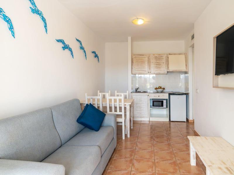 Compacte woonkamer met grijze bank, muurdolfijnen en kleine keuken met eettafel.