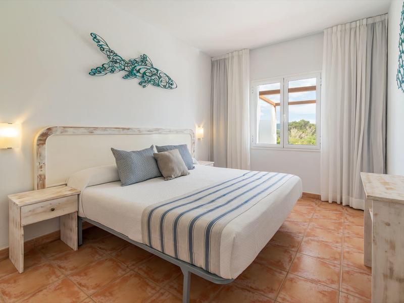 Lichte slaapkamer met witte muren, tegelvloer, tweepersoonsbed, nachtkastjes en wanddecoratie.