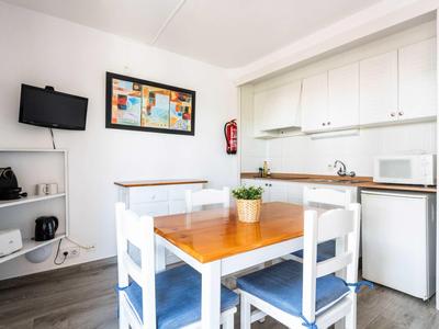 Piccola angolo cottura luminosa con tavolo da pranzo, sedie, TV e attrezzature moderne in un appartamento vacanze.