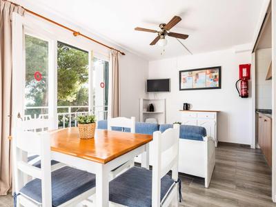 Zona pranzo luminosa con tavolo in legno, sedie e accesso al balcone con vista sul verde.