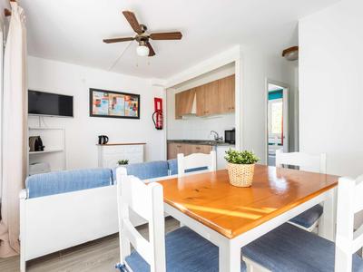 Soggiorno e zona pranzo luminosi con tavolo in legno, sedie bianche, divano e cucina moderna.