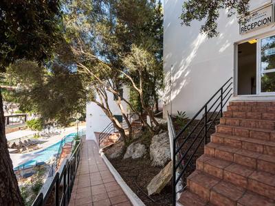 Esterno dell'hotel con piscina, alberi, scale e porta della reception alla luce del giorno.
