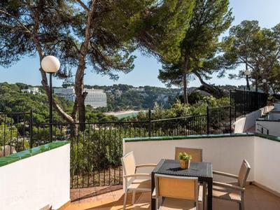 Balcone con tavolo e sedie, circondato da muri bianchi e vista su colline boschive.