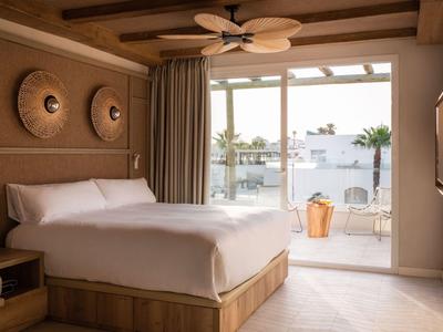 Helles Hotelzimmer mit Doppelbett, Deckenventilator und Zugang zu Balkon mit Meerblick.