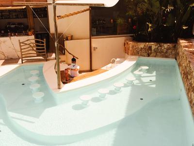 Outdoor pool with built-in stools and a child playing near a shaded area with seating.
