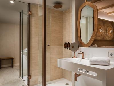 Modern hotel bathroom with glass shower, white sink, wooden mirror frame, and towel on counter.