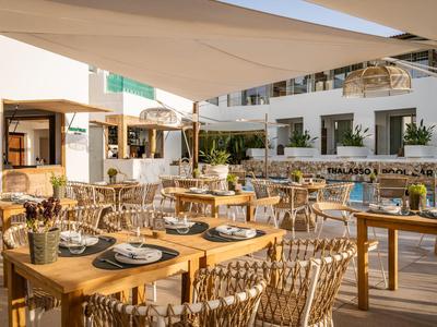 Freiluftrestaurant mit Holztischen, geflochtenen Stühlen und Blick auf einen Hotelpool.