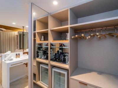 Moderner Hotelzimmer-Schrank mit Regalen, Mini-Kühlschrank und offener Garderobe in neutralen Farben.