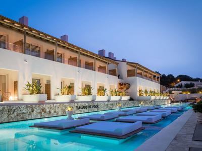 Modern hotel terrace with sunbeds by an illuminated pool during dusk.