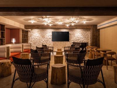 Cozy lounge area with wicker chairs, wooden stools, and warm lighting in a hotel setting.