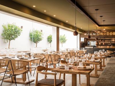 Modernes Restaurant mit Holztischen, Stühlen und dekorativen Bäumen an der Wand.