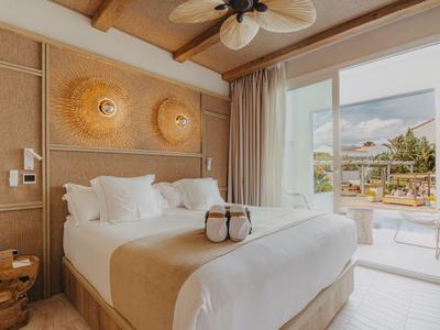Ein helles Hotelzimmer mit Doppelbett, dekorativen Wandlampen und Blick auf eine Terrasse.