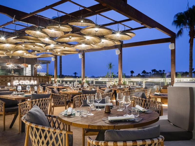 Outdoor restaurant seating with tables and chairs under a decorative canopy during twilight.