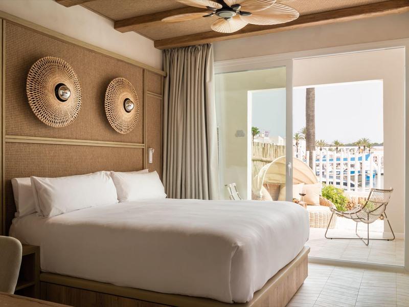 Modern hotel room with large bed, earthy decor, and sliding glass doors to a balcony.