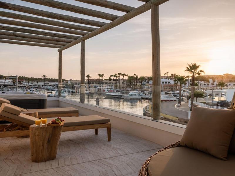 Cozy terrace with lounge chairs overlooks a marina at sunset.