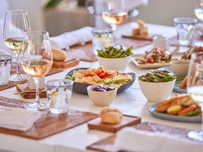 Elegant gedekte eettafel met wijn, salades en broodmanden in een lichte ruimte.