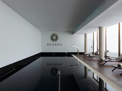 Modern binnenzwembad met ligstoelen en grote ramen die daglicht binnenlaten.