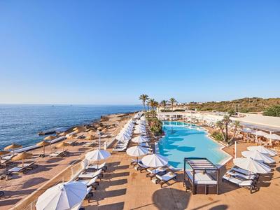 Helderblauwe zee en lucht, zwembad met ligbedden en parasols op een terras