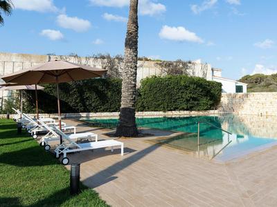 Zwembad met witte ligstoelen, parasol en groen gazon onder een blauwe lucht.