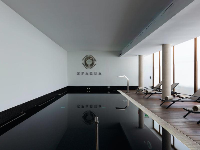 Modern binnenzwembad met ligstoelen en grote ramen die daglicht binnenlaten.