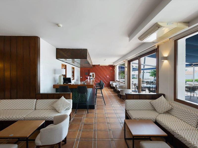 Lichte lobby met comfortabele banken, houten accenten en grote ramen met uitzicht op het terras.