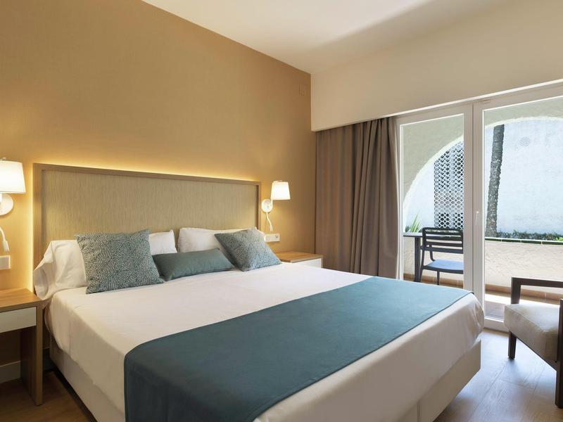 Modern hotelkamer met groot bed, wandlampen en toegang tot terras.