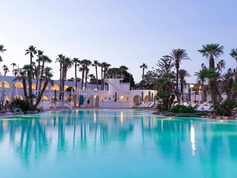 Groot zwembad voor een hotel met palmbomen en heldere avondlucht.