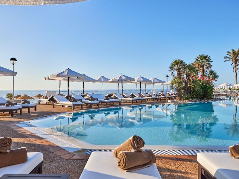 Rustige zwembadzone met ligstoelen, parasols en uitzicht op zee bij zonsondergang.