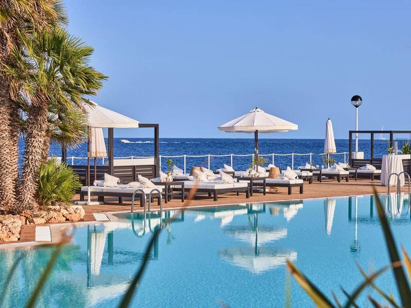 Luxe zwembadgebied met ligstoelen en parasols met uitzicht op zee onder een heldere lucht.