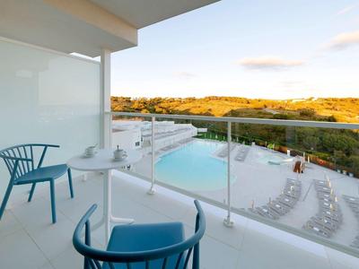 Nowoczesny balkon hotelowy z widokiem na basen i przyrodę o zachodzie słońca.