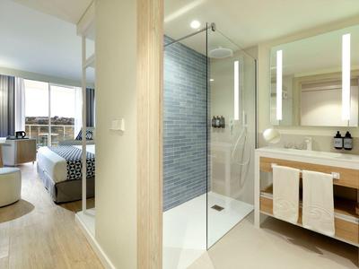 Jasny pokój hotelowy z nowoczesną łazienką z prysznicem i umywalką.