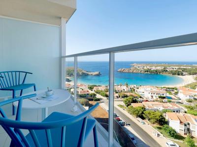 Nowoczesny balkon z niebieskimi krzesłami i widokiem na morze oraz miasto poniżej.