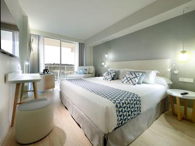 Nowoczesny pokój hotelowy z dużym łóżkiem, naturalnym światłem i minimalistycznym wyposażeniem.