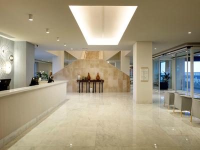 Nowoczesny hol hotelowy z błyszczącą podłogą, recepcją i siedzeniami obok dużych okien.