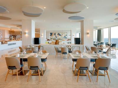 Jasna jadalnia z eleganckimi stołami, nowoczesnymi krzesłami i dużymi oknami.