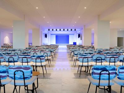 Duża jasna sala konferencyjna z wieloma niebieskimi krzesłami i sceną z przodu