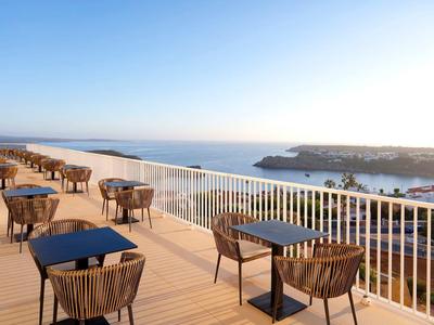 Drewniany taras z stolikami i krzesłami z widokiem na morze i niebieskie niebo.