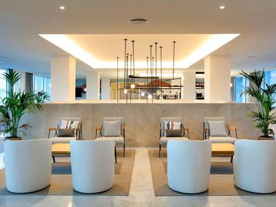 Nowoczesny lobby hotelowe z białymi siedziskami i dużymi zielonymi roślinami.