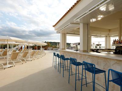 Bar na świeżym powietrzu z niebieskimi stołkami i leżakami pod parasolami w hotelu.