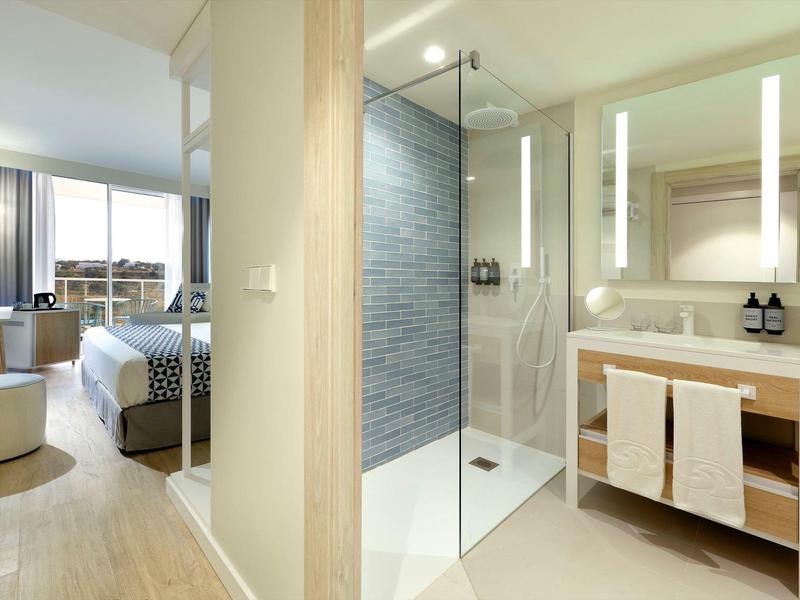 Jasny pokój hotelowy z nowoczesną łazienką z prysznicem i umywalką.