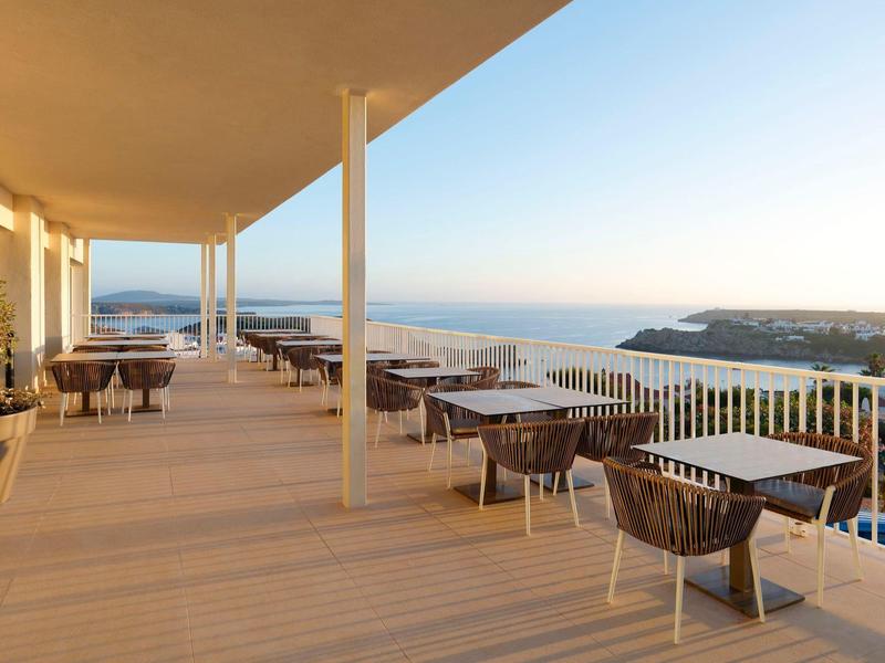 Taras hotelowy z stolikami i widokiem na morze o zachodzie słońca.