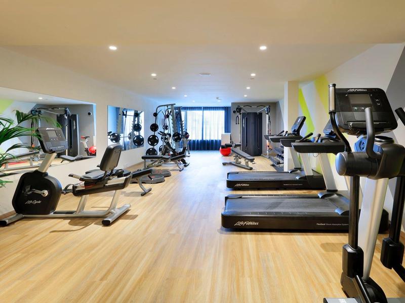 Nowoczesna siłownia z bieżniami i różnym sprzętem, jasna drewniana podłoga.