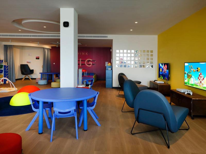 Nowoczesna sala rekreacyjna z niebieskimi stołami, fotelami i telewizorami.