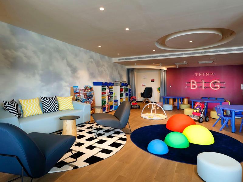 Nowoczesny salon z niebieskimi fotelami, czarno-białym dywanem, ścianą z chmurami, kolorową strefą zabaw.