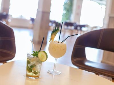 Due cocktail su un tavolo bianco in un bar luminoso con sedie sullo sfondo.