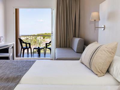 Camera d'hotel moderna con letto, divano e balcone con vista sul verde.