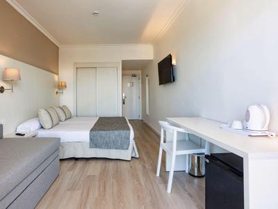 Camera d'hotel moderna con letto, divano, scrivania e TV a parete.