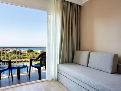 Camera d'hotel con divano e balcone con vista sul mare e sul giardino